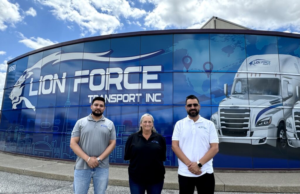 Lion Force's two owners and a general manager outside of the headquarters in Mississauga, Ont, in front of the banner with the logo